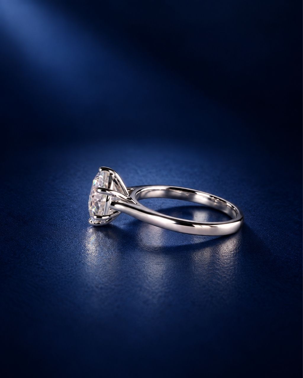 Side view of a 6-prong round moissanite solitaire engagement ring in polished 14K solid white gold, showcasing the raised basket setting and slender band on a deep navy blue background.