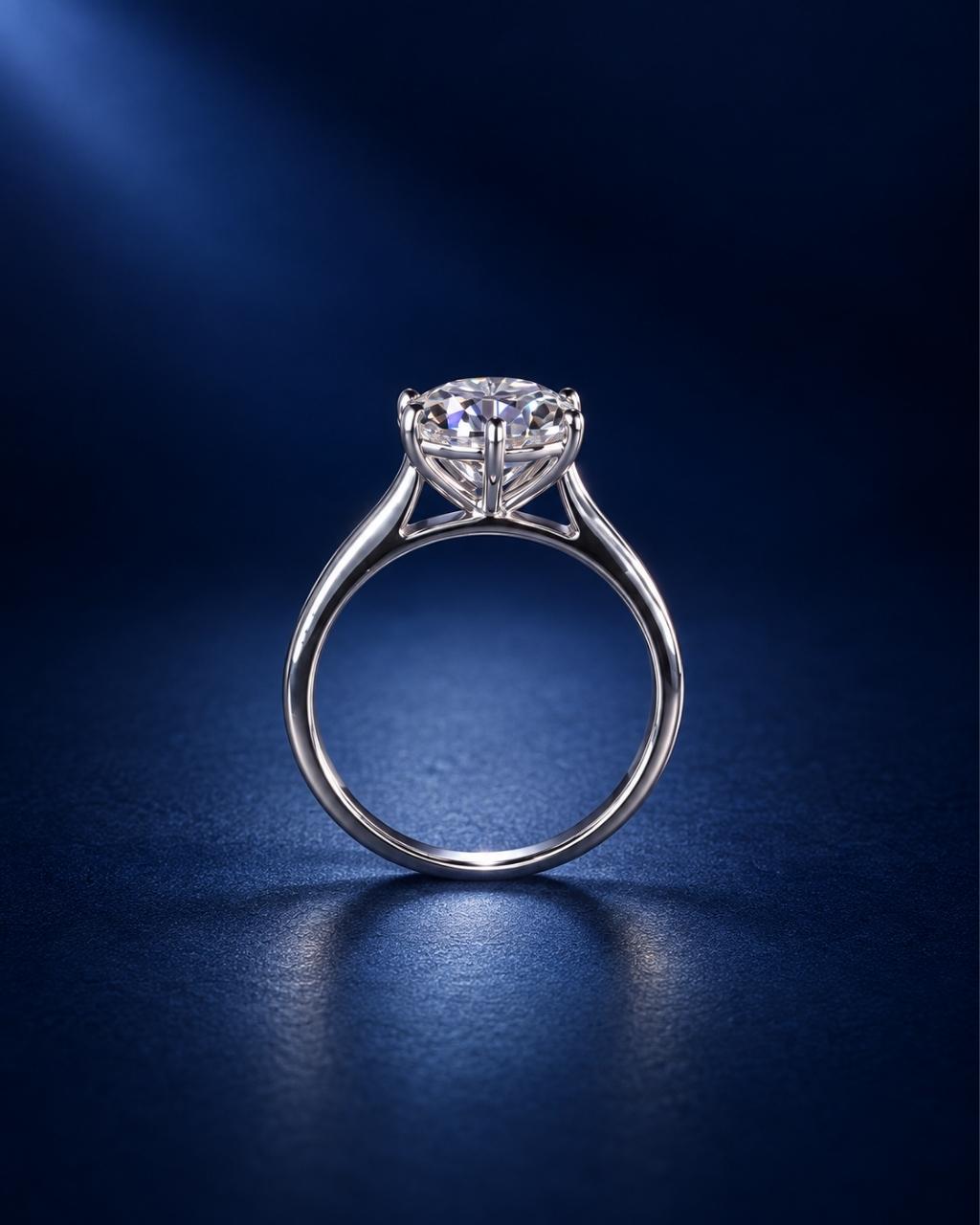 Standing side view of a 6-prong round moissanite solitaire engagement ring in polished 14K solid white gold, showcasing the elevated basket setting and slender band on a deep navy blue background.