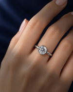 Round bezel-set moissanite solitaire ring in polished 14K solid white gold worn on a female hand, featuring a brilliant round-cut stone against a deep navy blue background