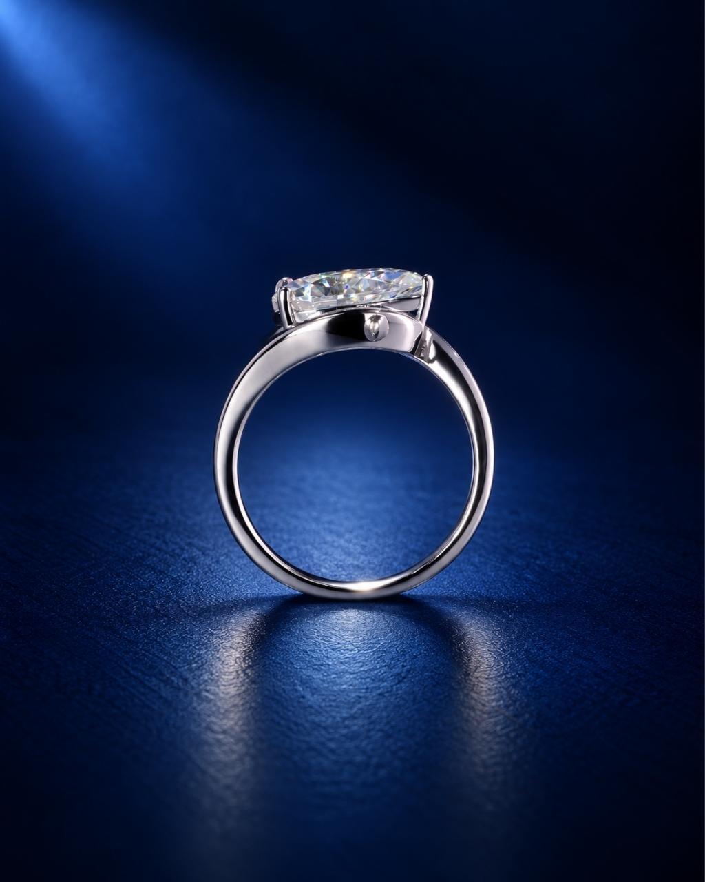 Side profile of a pear-cut moissanite engagement ring in polished white gold, highlighting the elevated stone setting and sleek band against a deep navy blue background.