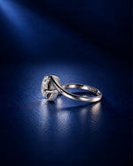 Side view of a pear-cut moissanite engagement ring in polished white gold, showcasing the sculptural swirl bypass setting and raised stone profile against a deep navy blue background.