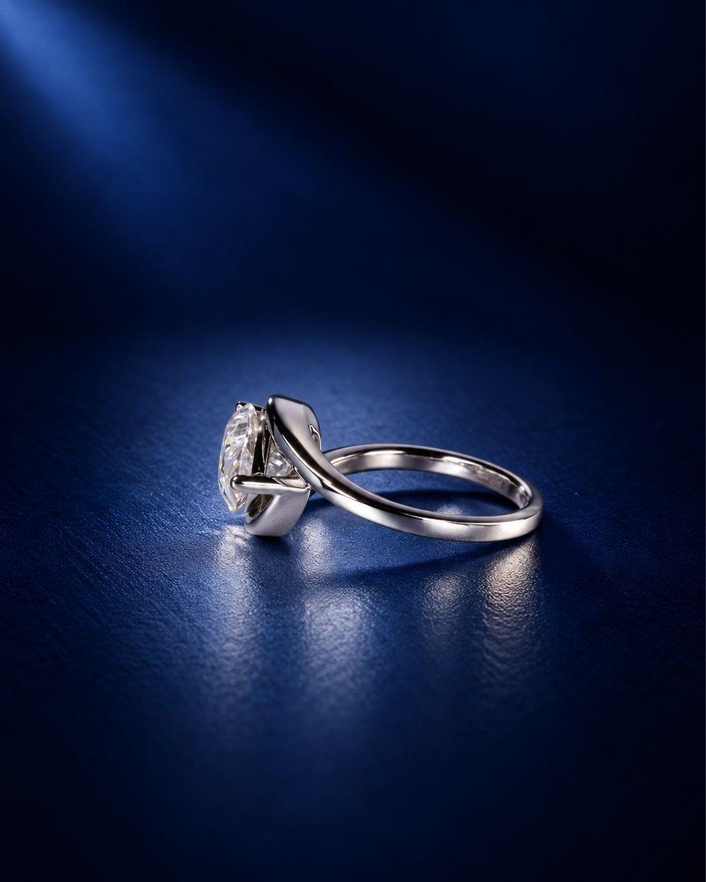 Side view of a pear-cut moissanite engagement ring in polished white gold, showcasing the sculptural swirl bypass setting and raised stone profile against a deep navy blue background.