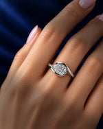 Pear-cut moissanite engagement ring in polished white gold with a modern swirl bypass setting, shown on a woman’s finger against a deep navy blue background.